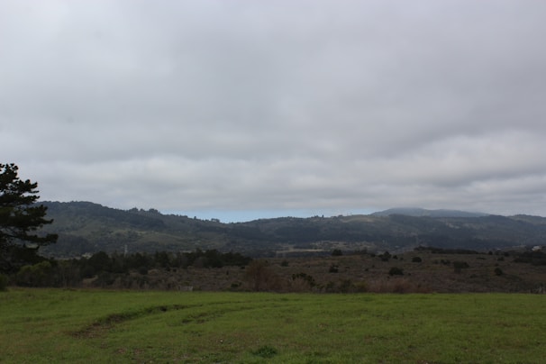 A wide-angle landscape of rolling hills under a cloudy sky.