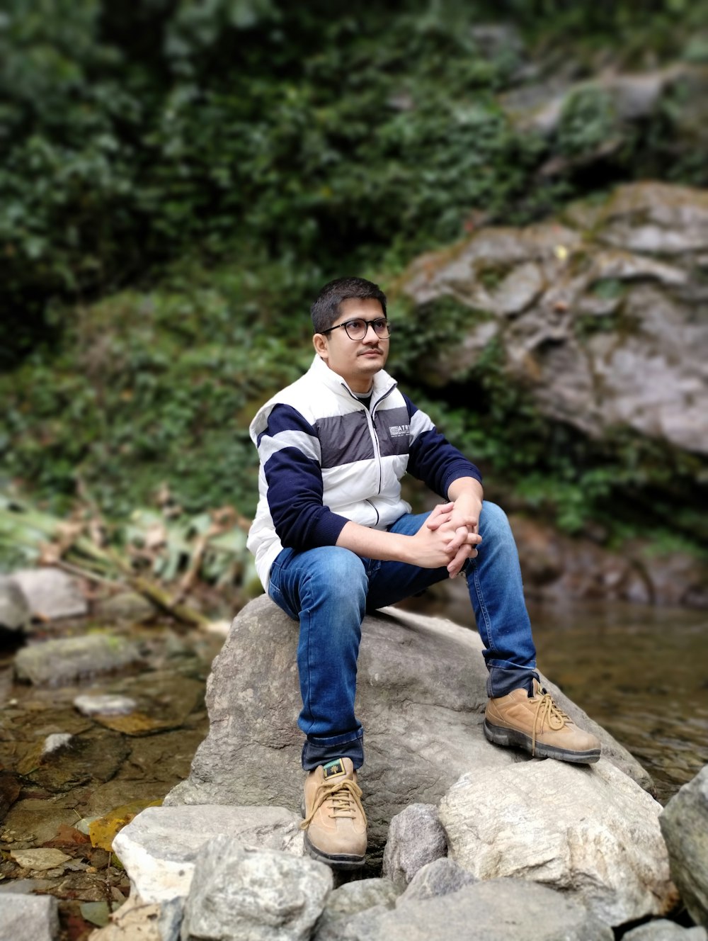 a man sitting on top of a rock next to a river