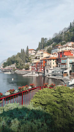 A vibrant lakeside village with colorful houses reflecting in the calm waters of Lake Reschen under a bright blue sky.