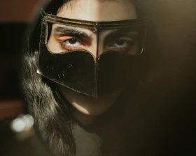 A shadowed figure wearing an elegant black mask, bathed in soft gold light, set against a dark, cinematic backdrop.