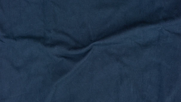 Close-up of textured fabric in midnight blue and ivory, highlighting subtle folds and shadows.