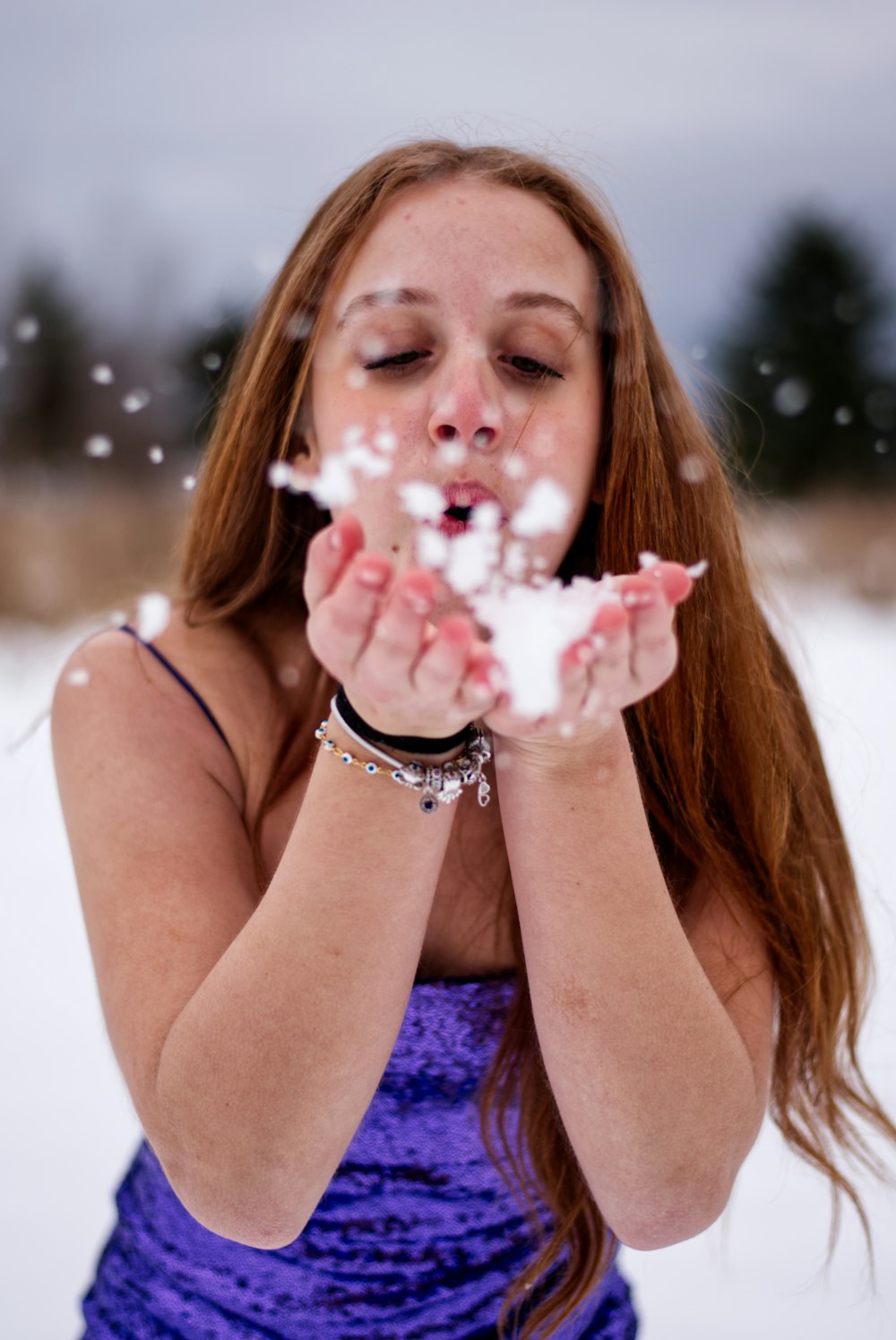 uma mulher soprando neve em suas mãos na neve