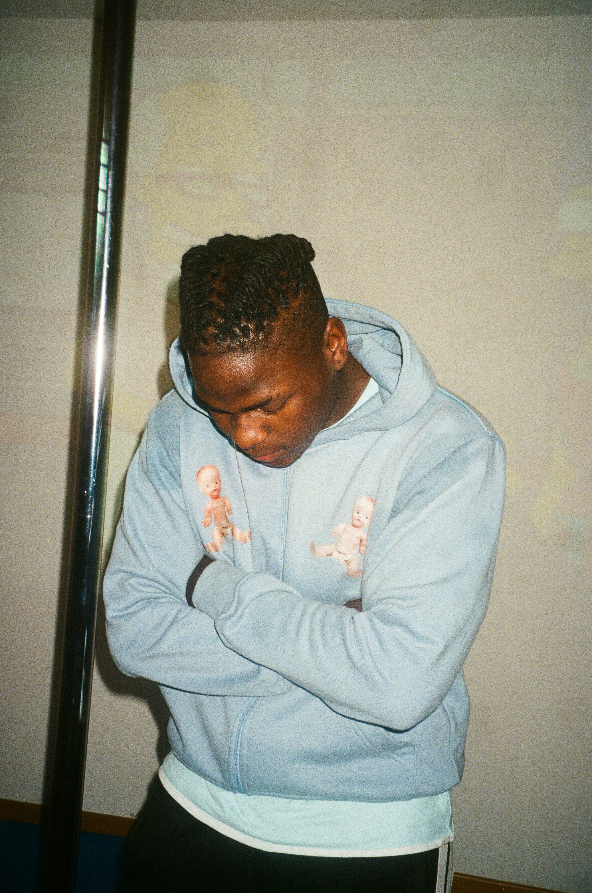 a man in a blue hoodie leaning against a pole