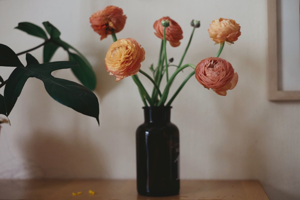 a black vase filled with flowers on top of a wooden table