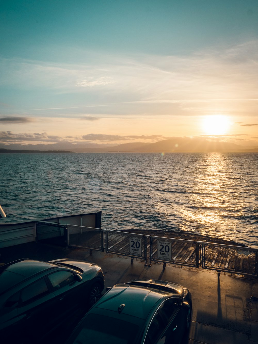 the sun is setting over the ocean as cars are parked on the dock