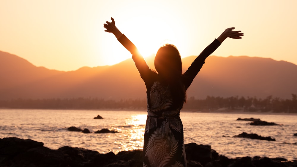 a woman standing on a beach with her arms outstretched