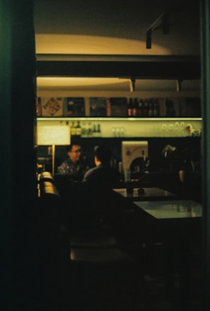 A dimly lit lounge where two people share a close, playful glance over cocktails.