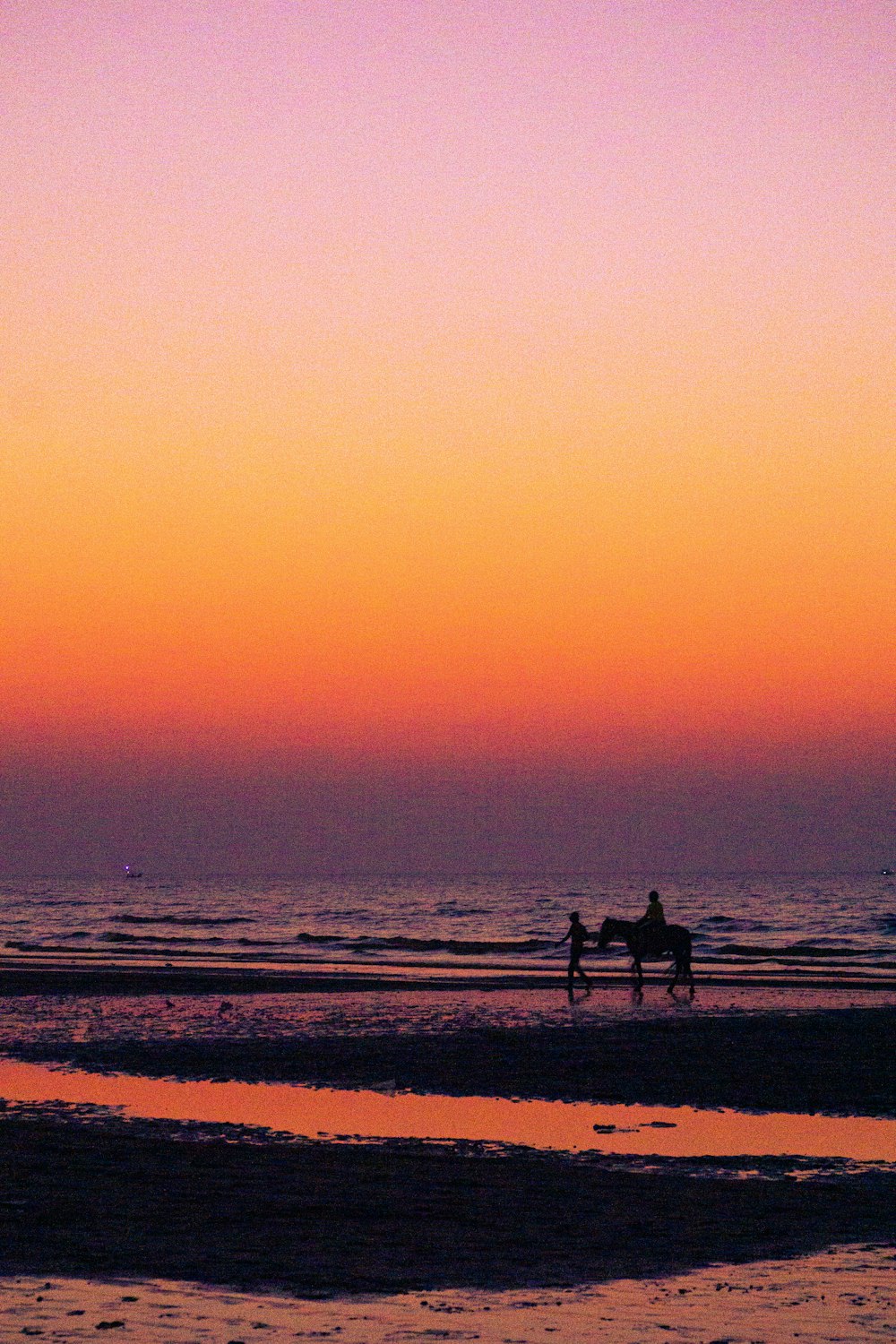 a couple of people riding horses on top of a beach