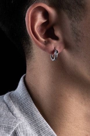 A fresh piercing with a sleek silver hoop on an ear against dark background.