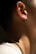 A close-up of a person's ear and neck is visible, featuring an earring on the ear and a chain necklace around the neck. The lighting creates soft shadows, highlighting the texture of the skin and jewelry.