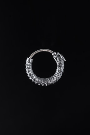 A silver spiked earring levitating gently against a pitch black background.