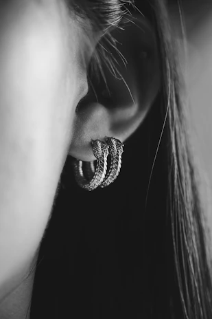 Black and white photo of a model wearing bold, angular earrings in a bright, spacious gallery setting