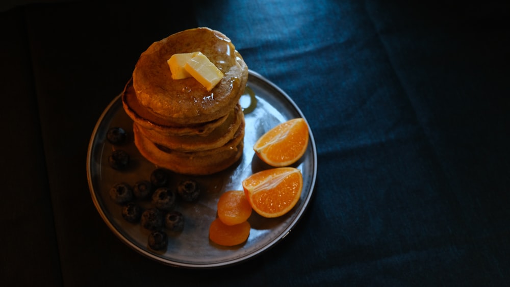 a stack of pancakes on a plate with orange slices and blueberries
