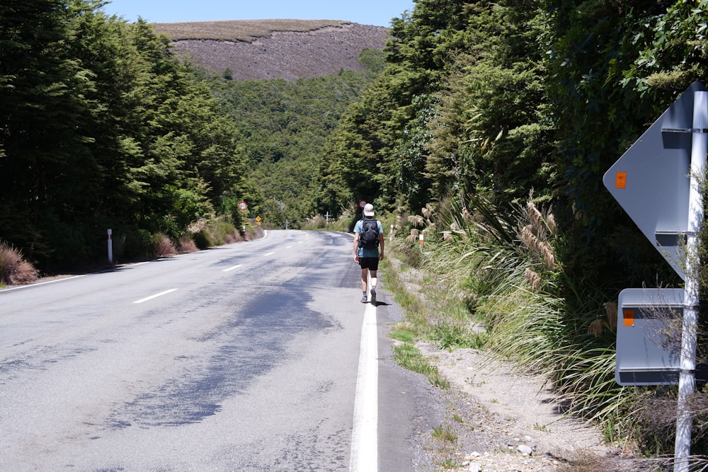 a man walking down a road next to a forest