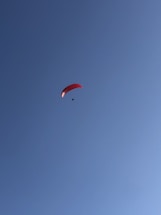 A lone paraglider with a red canopy soars against a clear blue sky, creating a sense of freedom and adventure.
