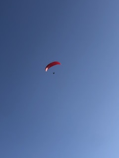 A lone paraglider with a red canopy soars against a clear blue sky, creating a sense of freedom and adventure.