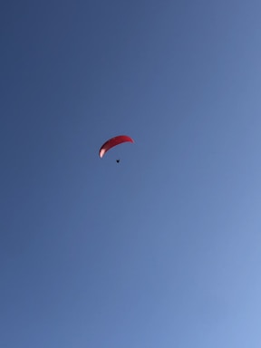 A lone paraglider with a red canopy soars against a clear blue sky, creating a sense of freedom and adventure.