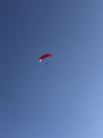 A lone paraglider with a red canopy soars against a clear blue sky, creating a sense of freedom and adventure.
