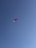 A lone paraglider with a red canopy soars against a clear blue sky, creating a sense of freedom and adventure.