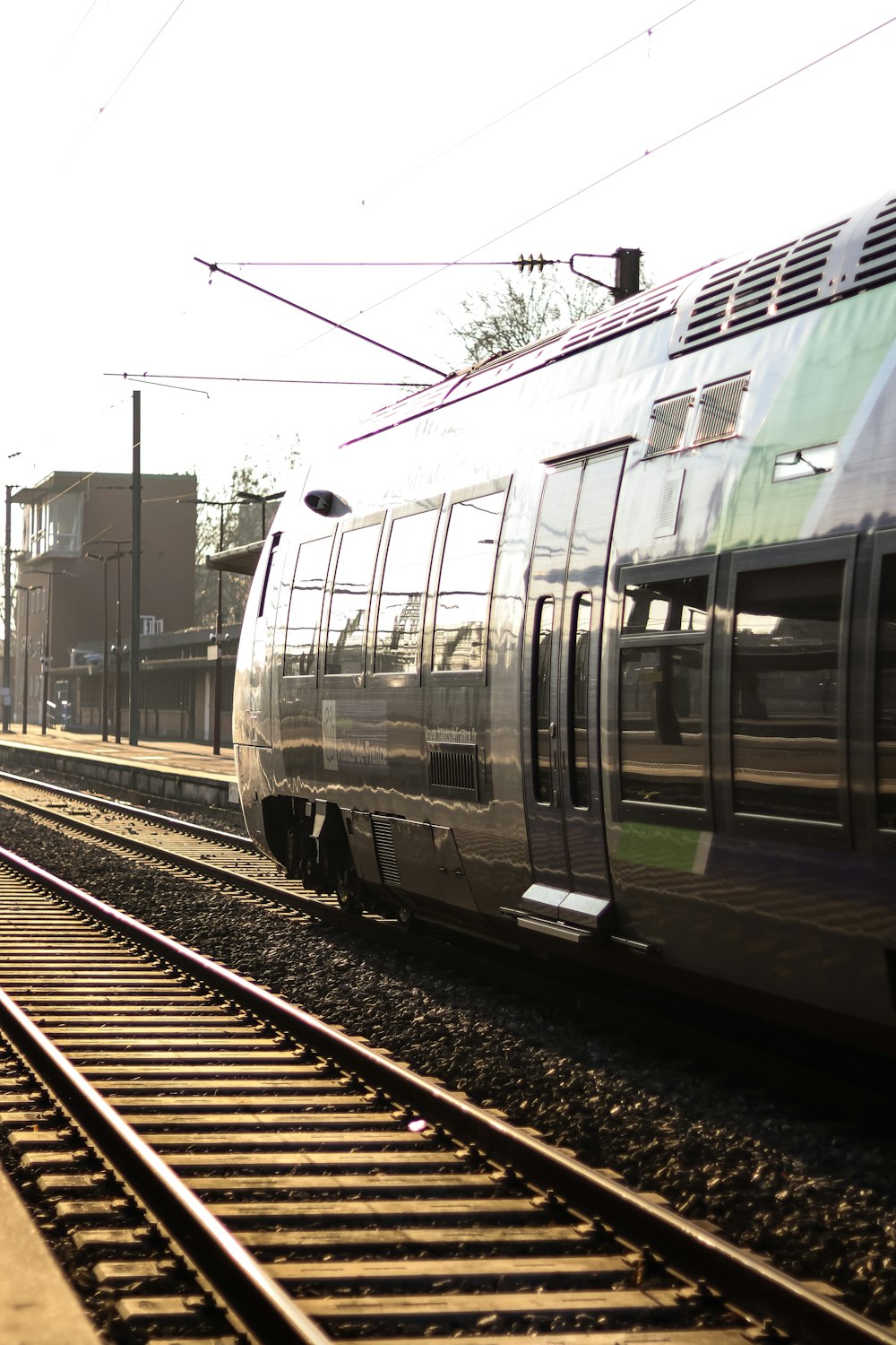 Ein silberner Zug, der neben einem Gebäude die Bahngleise hinunterfährt