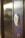 A close-up view of a modern electronic door lock with a circular design, featuring a green illuminated button. The lock is installed on a wooden surface, and the background is softly blurred.