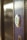A close-up view of a modern electronic door lock with a circular design, featuring a green illuminated button. The lock is installed on a wooden surface, and the background is softly blurred.