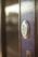 A close-up view of a modern electronic door lock with a circular design, featuring a green illuminated button. The lock is installed on a wooden surface, and the background is softly blurred.