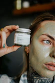 a woman holding a jar of clay on her face