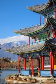 a chinese building with red pillars and a lake in front of it