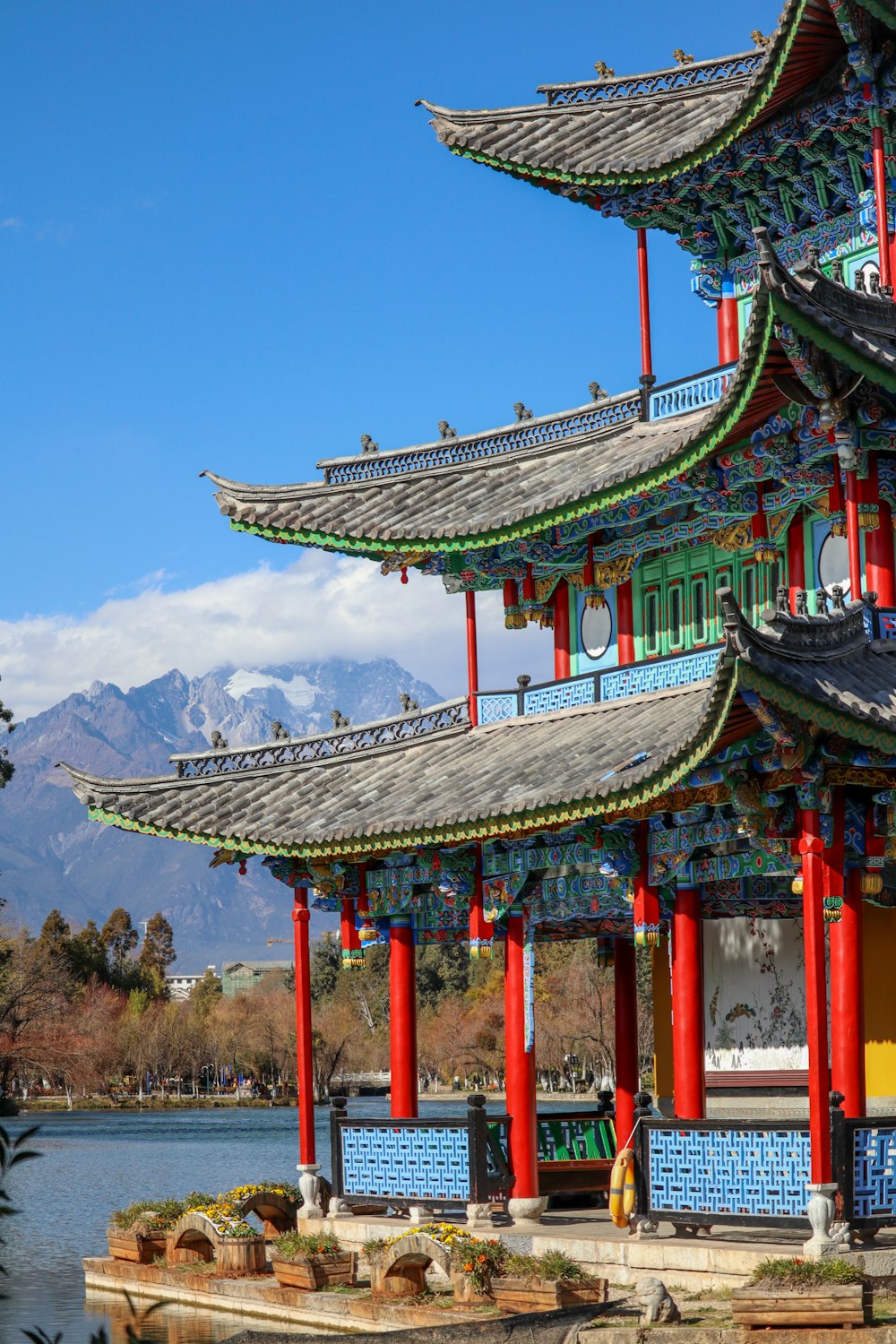 a chinese building with red pillars and a lake in front of it