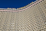 A large architectural structure with a detailed facade composed of a repeating pattern of square and rectangular windows. The building has a prominent signage at the top in bold letters spelling 'HOTEL UZBEKISTAN' against a clear blue sky.