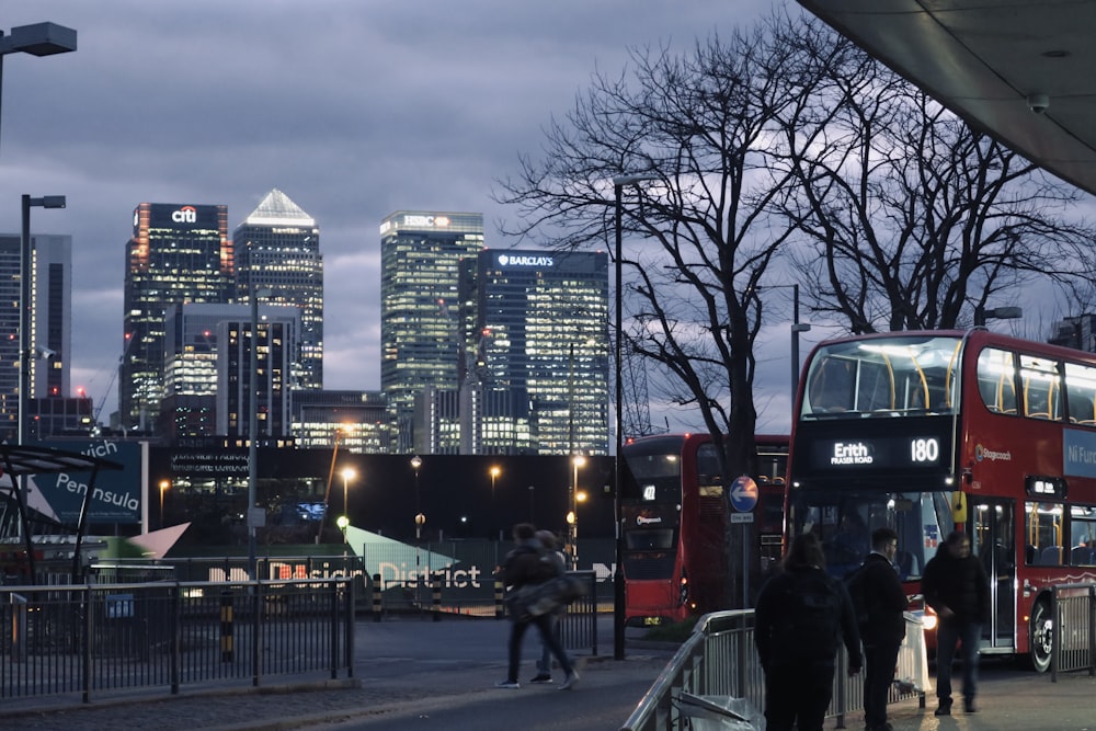 a group of people walking down a sidewalk next to a red double decker bus