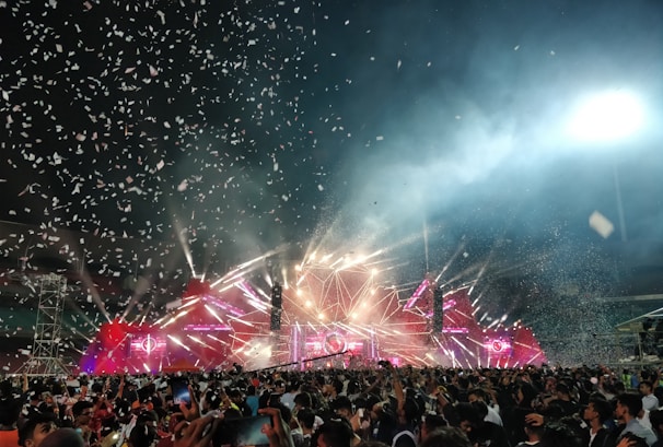A joyful crowd enjoying a live show with banners of Multiverso Geek and the Stark Innovations partnership glowing in the background.