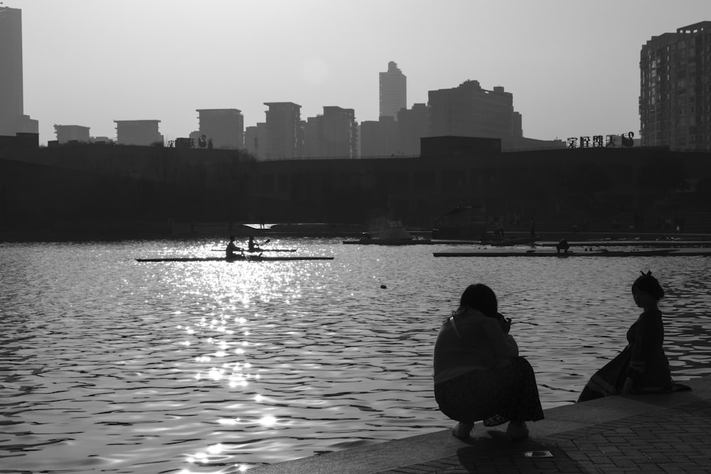 two people sitting on the edge of a body of water