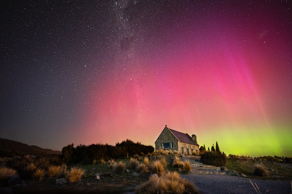 Una casa con una luz de aurora rosa y verde en el fondo