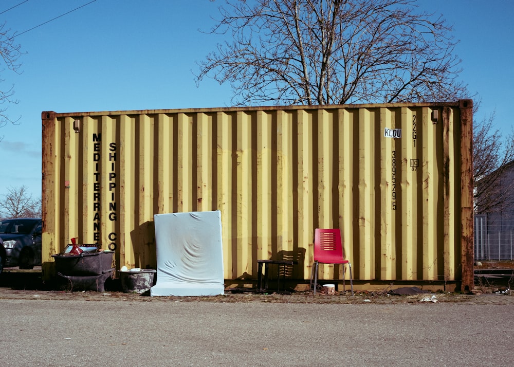 a yellow shipping container sitting next to a red chair
