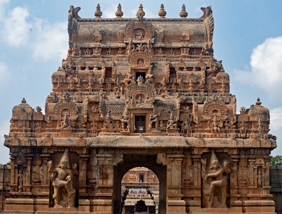 An intricately carved temple entrance with detailed sculptures and ornate designs depicting deities and mythological figures. The structure exhibits classical architecture with tiered levels and decorative motifs.