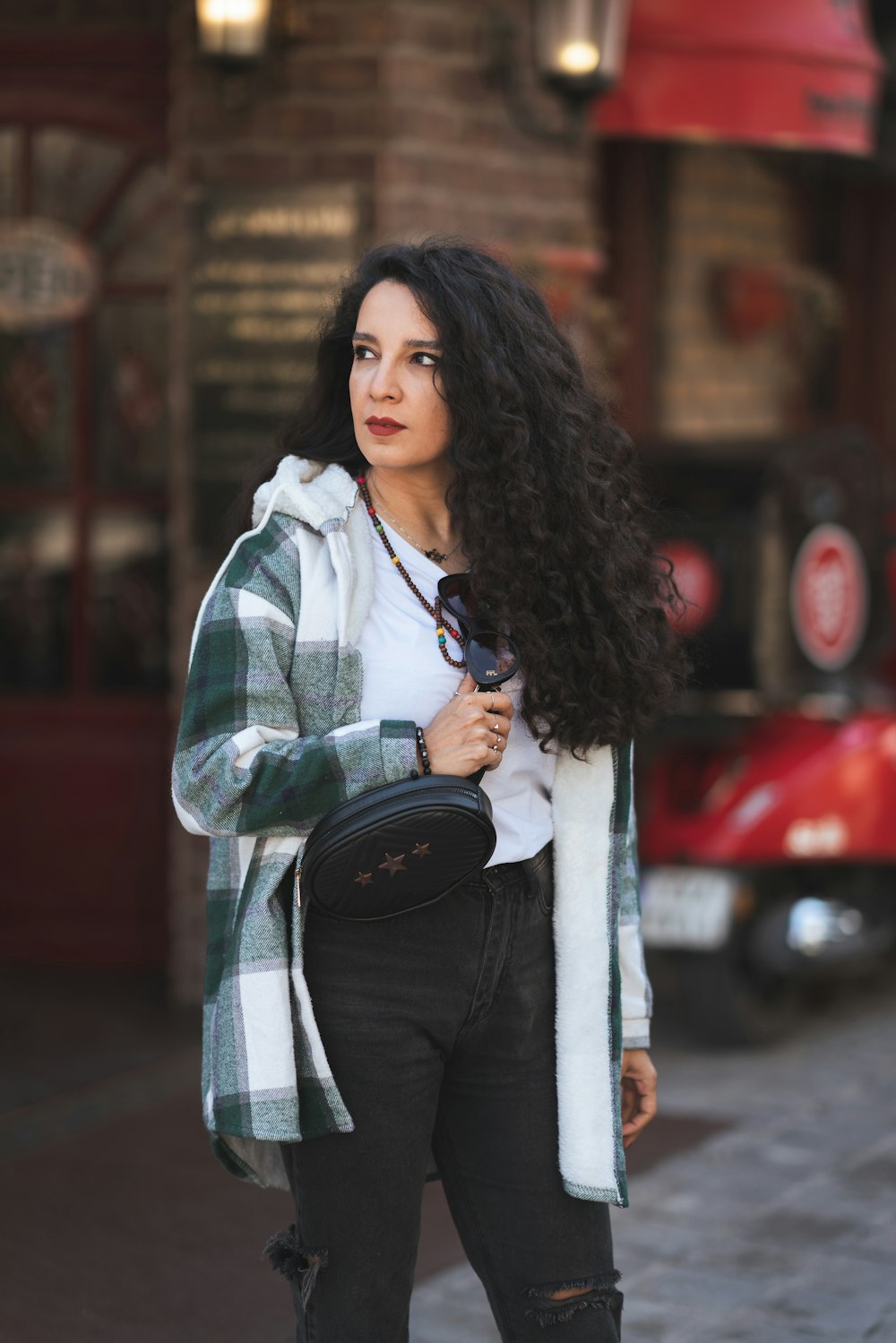 a woman with long black hair is standing on a sidewalk