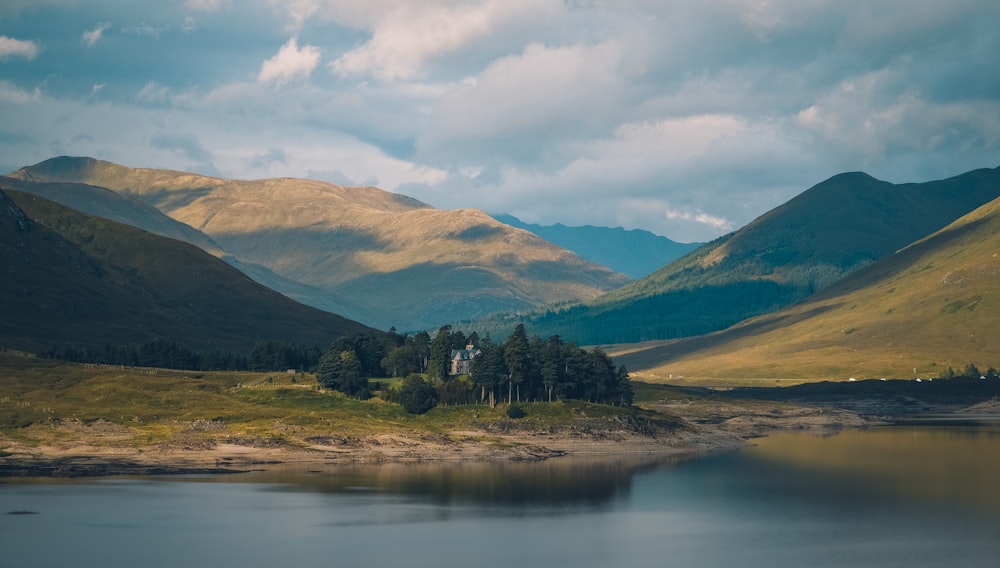 a lake surrounded by mountains under a cloudy sky