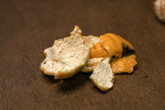 Close-up of vibrant orange peel powder spilling from a wooden bowl onto a rustic surface, highlighting its natural texture.