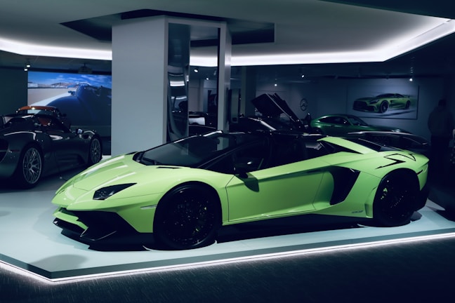 A sleek, lime green sports car is displayed in a well-lit showroom. The car's doors are open, showcasing its luxurious interior. In the background, other high-performance vehicles are partially visible, creating an atmosphere of elegance and sophistication.
