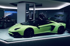 A sleek, lime green sports car is displayed in a well-lit showroom. The car's doors are open, showcasing its luxurious interior. In the background, other high-performance vehicles are partially visible, creating an atmosphere of elegance and sophistication.