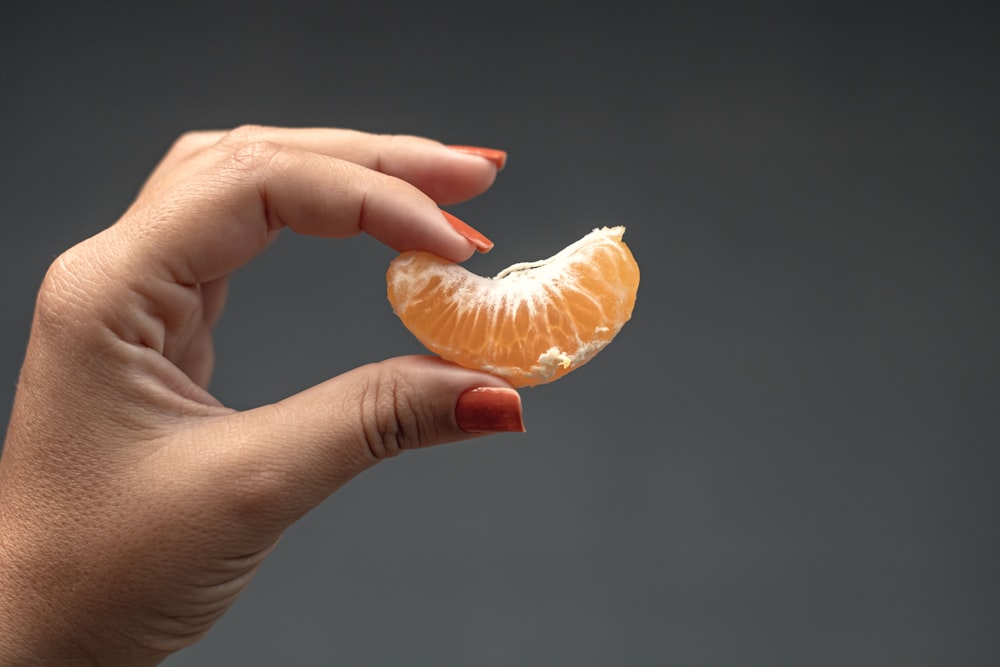 a mão de uma mulher segurando uma fatia laranja