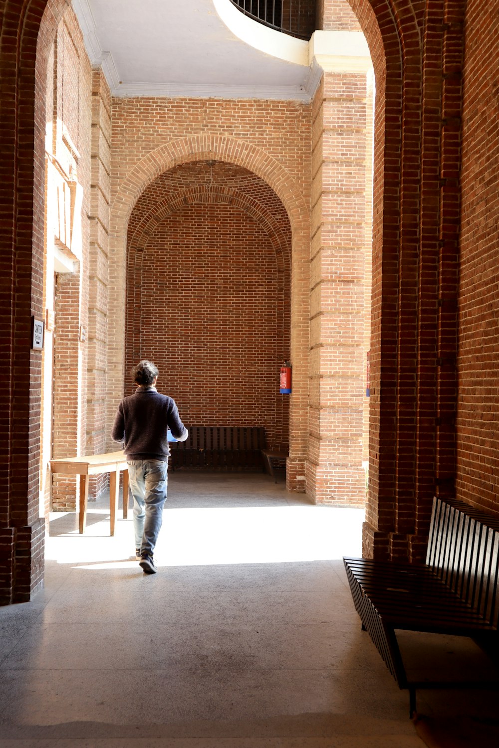 a man walking down a hallway between two benches