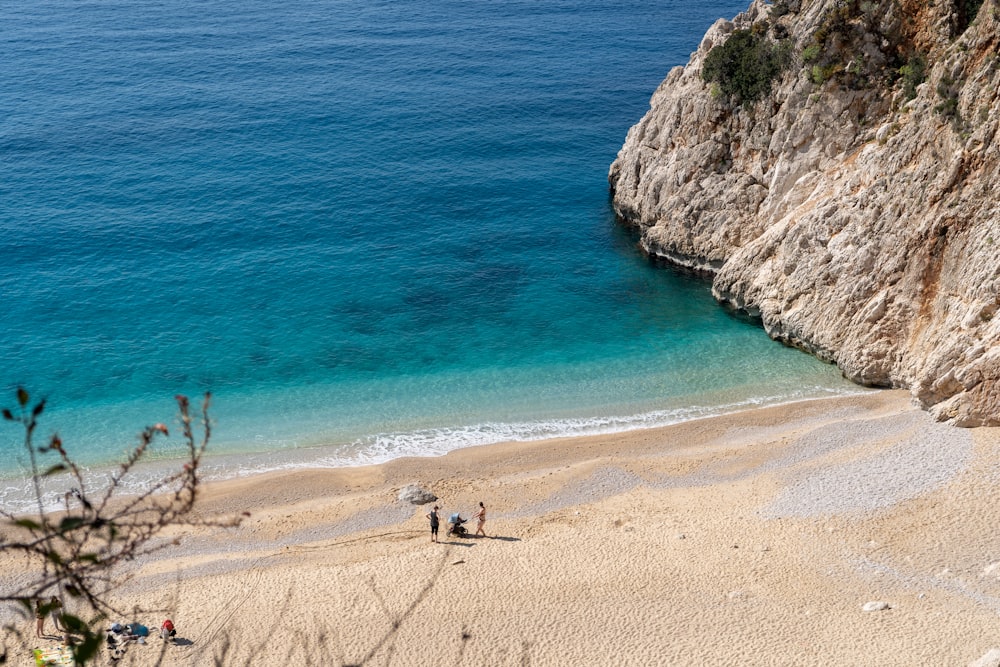 a beach with people walking on it next to a cliff