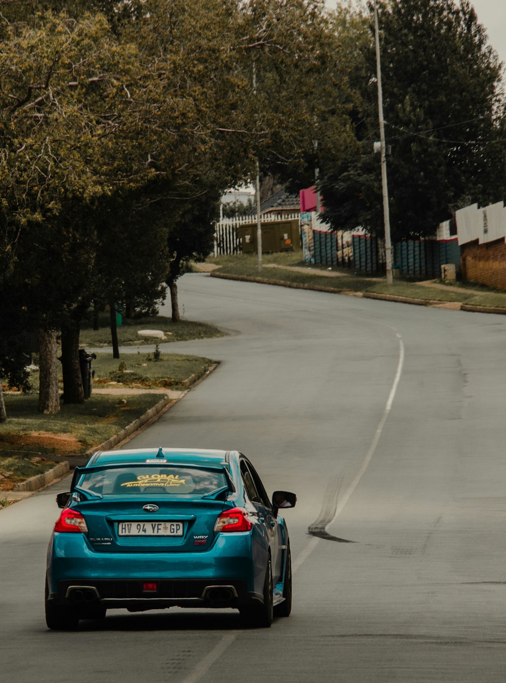 a blue car driving down a street next to trees