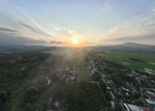 An aerial view of a rural village with new infrastructure projects underway, framed by the deep orange sunset.