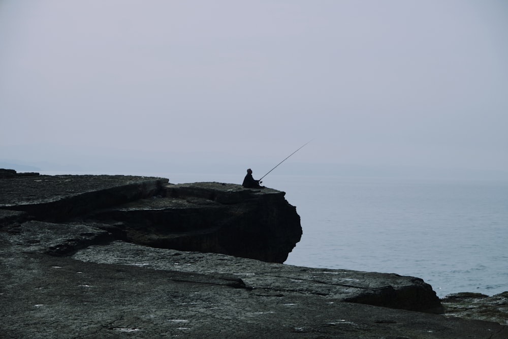 a man sitting on a rock with a fishing rod