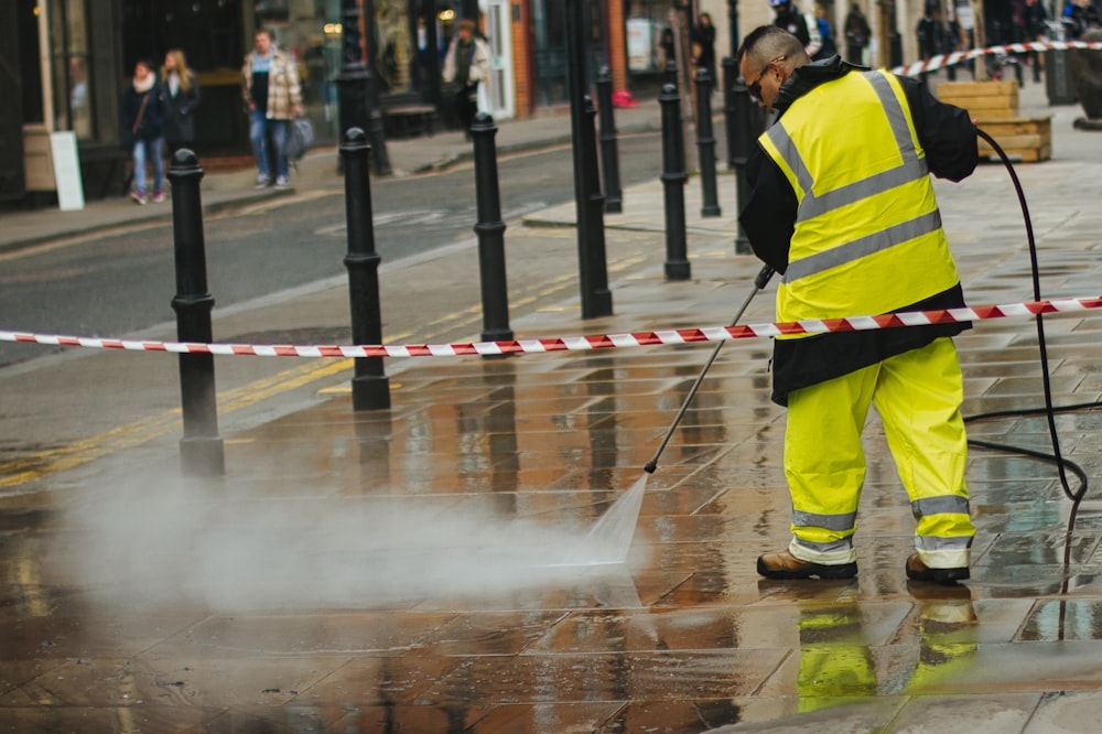 a man in a yellow jacket is using a pressure washer