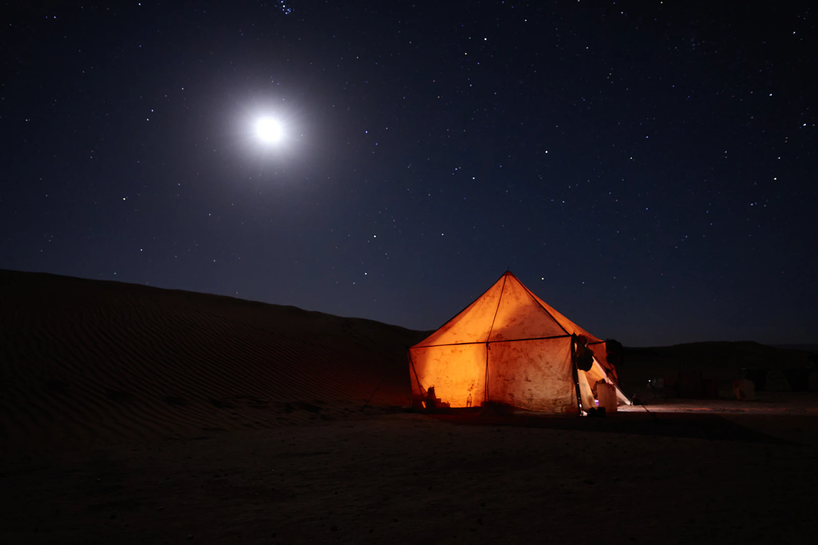 A tent standing alone in the desert beneath a starlit night sky